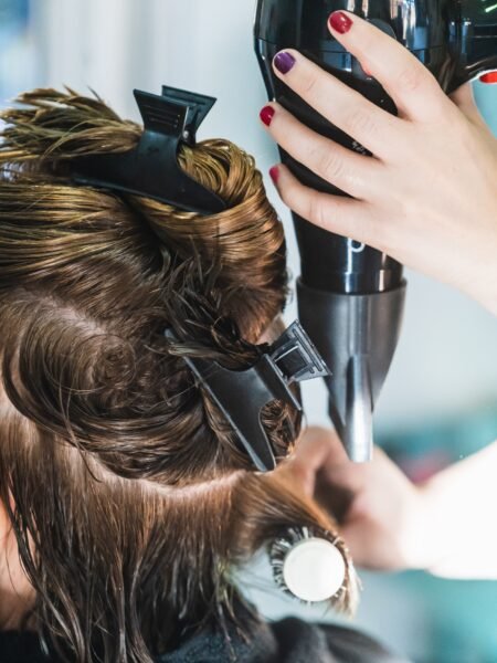 A vertical closeup shot of a hairdresser blow drying a woman's short hair in a beauty salon